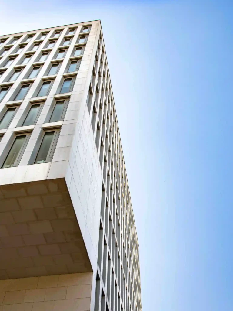 Fotograf Hannover Untersicht eines modernen, hohen Gebäudes mit einem gitterartigen Fenstermuster an der Fassade vor einem klaren blauen Himmel. Das Gebäude scheint ein Büro- oder Geschäftsgebäude mit einem schlanken, minimalistischen Design zu sein. Fotograf in der Nähe.