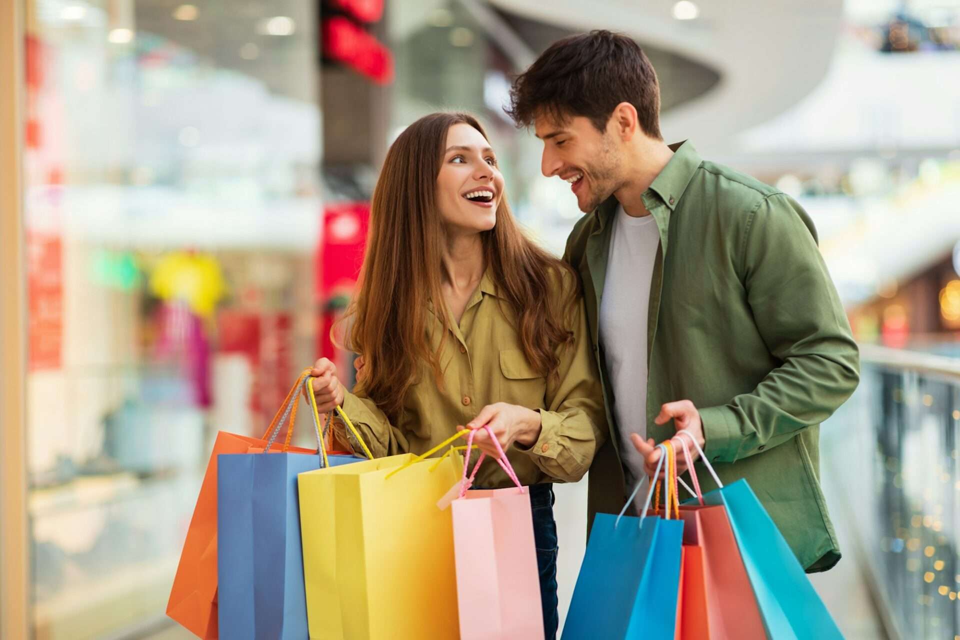 Joyful Couple On Shopping Laughing Holding Shopper Bags In Hypermarket